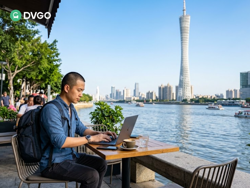 Digital nomad using laptop at a Guangzhou riverside cafe with the Canton Tower in the background